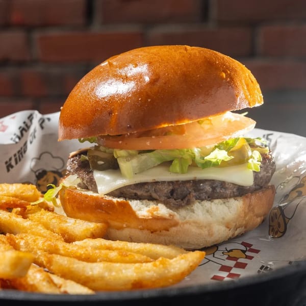 A Halftime Pizza burger with cheese, lettuce, tomato, and pickles, served with fries.