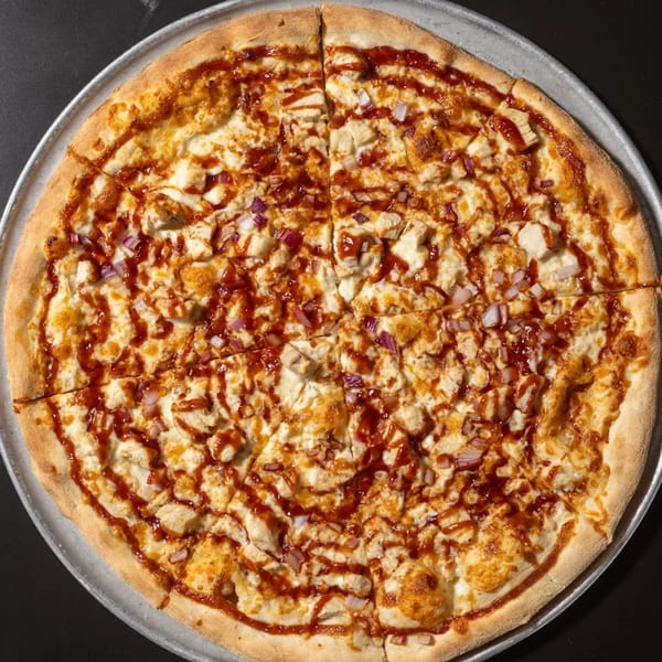 A whole Halftime Pizza BBQ chicken pizza, topped with red onions and a BBQ sauce drizzle.
