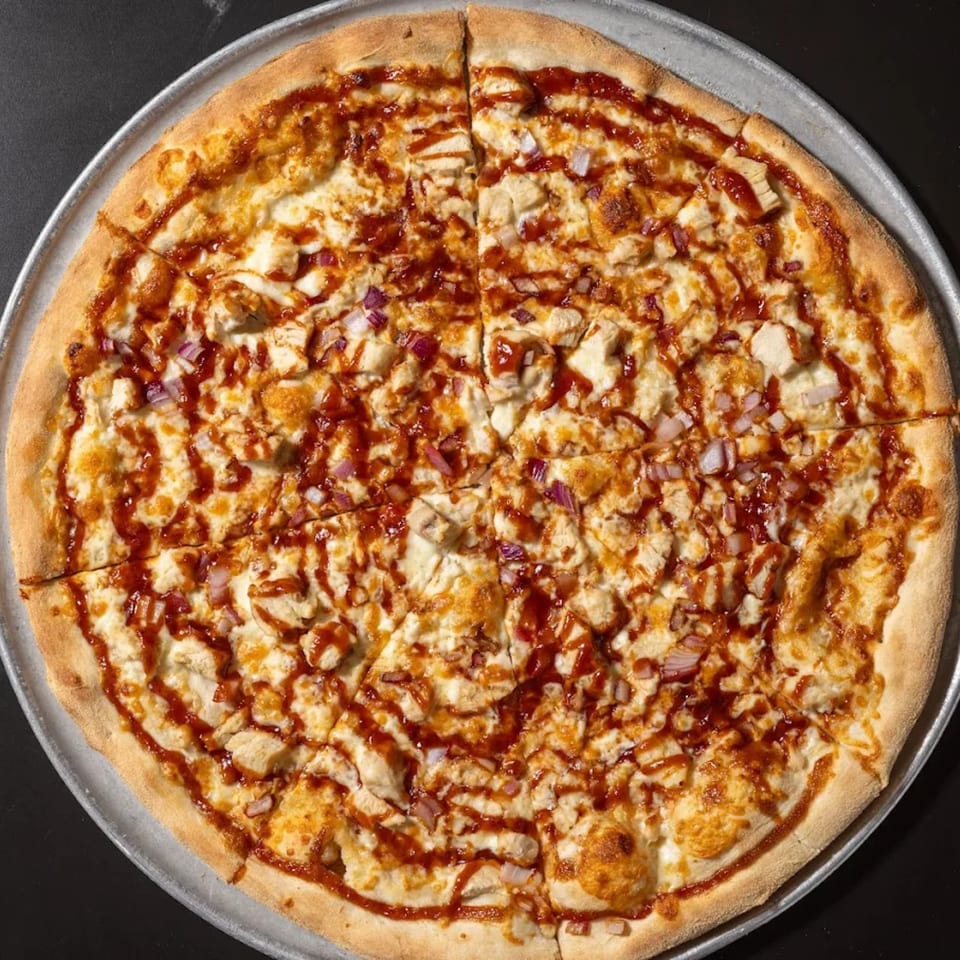 A whole Halftime Pizza BBQ chicken pizza, topped with red onions and a BBQ sauce drizzle.