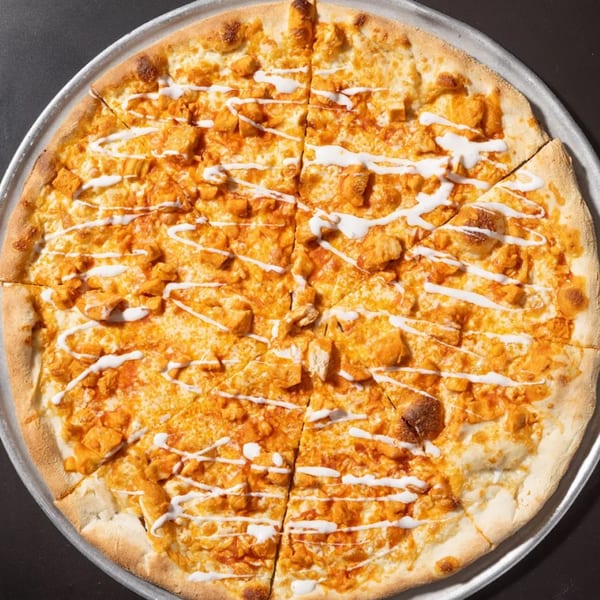 A whole Halftime Pizza buffalo chicken pizza, sliced, with white sauce drizzled over the top.