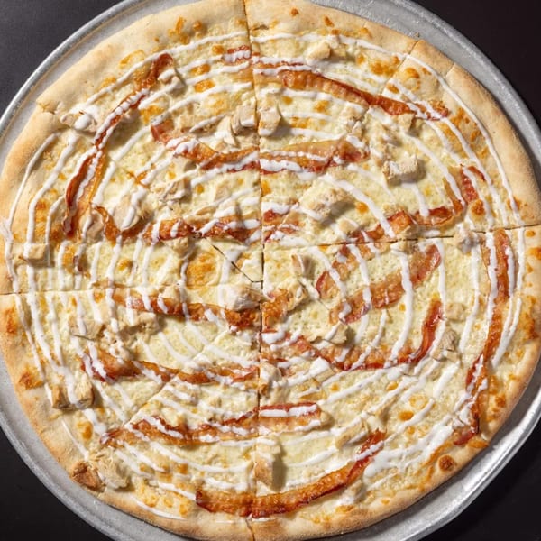 A whole Halftime Pizza with white sauce, chicken, and bacon, drizzled with ranch dressing.