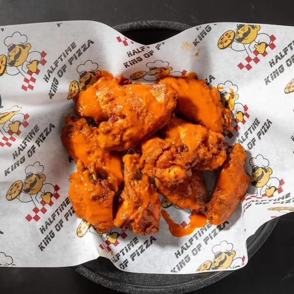 Halftime Pizza's buffalo wings, coated in bright orange sauce, served in a basket lined with branded paper.